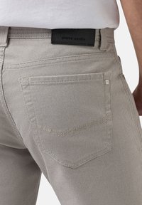 Hellgraue Denim-Jeans mit strukturiertem Finish, versehen mit einem schwarzen Lederetikett und klassischen Gesäßtaschen mit dezenten Nähdetails.