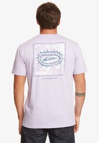 Light purple cotton t-shirt featuring a graphic design on the back with blue text and logo, short sleeves, and a relaxed fit.
