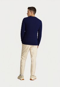 Navy blue cable-knit sweater, fitted design, ribbed hem and cuffs, paired with beige trousers and light-colored sneakers.