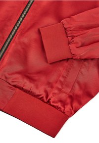 Czerwona kurtka bomberka wykonana z gładkiego, błyszczącego materiału, z prążkowanymi mankietami i zapięciem na zamek błyskawiczny z metalicznymi detalami. Minimalistyczny design bez wzorów.