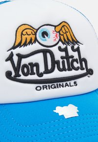 Sinine ja valge trucker peakate, millel on tikkitud logo, millel on silm ja tiivad. Valge esipaneel ja sinine võrkpaneel tagaküljel, millel on nööpregulaator.