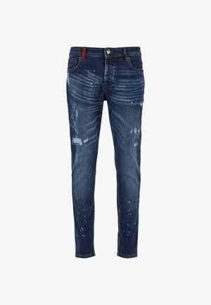 Tumedast sinisest denimist kitsad teksad, millel on kulumisjäljed, õrn pleekimine ja punane detail vööl.