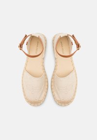 Beige espadrille sandals with circular embroidered pattern, jute sole, and brown ankle strap with gold-tone buckle. Soft textured fabric.