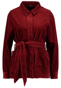 Rode corduroy jas met een kraag, lange mouwen, zijzakken en een strikceintuur. Beschikt over een verticale ribbelstructuur en een knoopsluiting.