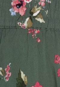 Tejido floral en verde oscuro con flores rosas y blancas. Textura fruncida con detalle elástico cerca de la parte superior y acabado suave y liso.
