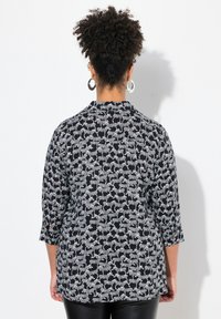 Sort skjorte med trekvartærmer, der har et hvidt zebra-mønster. Stoffet er glat med en afslappet pasform og detaljer med slids på ryggen.