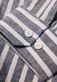 Camisa a rayas con líneas horizontales azul marino y blancas, con botones blancos, un cuello y una tela texturizada. Detalle de costura armoniosa.