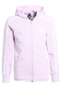 Haut de survêtement zippé rose pâle avec une capuche, bandes blanches sur les manches et poches avant. Fabriqué en tissu doux et texturé.