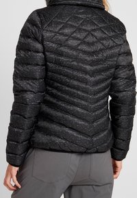 Svart vadderad pufferjacka med ett chevronmönster, hög krage och textilmaterial. Den har en figurnära silhuett och rundad nederkant.