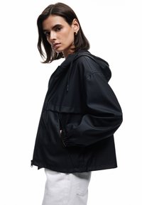 Zwarte hooded jack met een rits aan de voorkant, elastische manchetten en een relaxed fit. Gemaakt van een gladde stof met een contrasterende bovennaad detail.