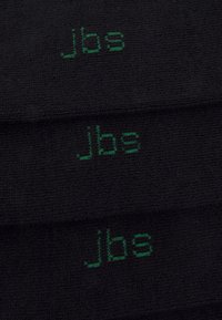 Schwarzer Stoff mit texturiertem Oberflächenbild zeigt wiederholt grünen, gestickten Text "jbs" in einer modernen, serifenlosen Schriftart.