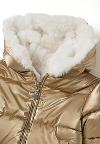 Glanzend gouden pufferjack met een witte nepbont gevoerde capuchon en gouden rits met een kleine hartvormige trekker.