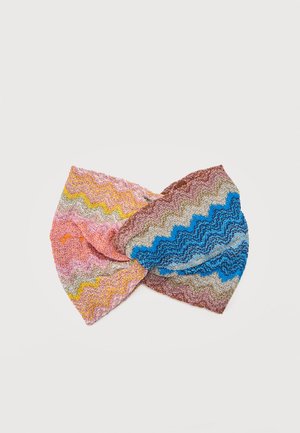 Bandeau en tricot avec un nœud torsadé, présentant un motif en zigzag rose, jaune, orange, bleu, beige et marron sur fond blanc.