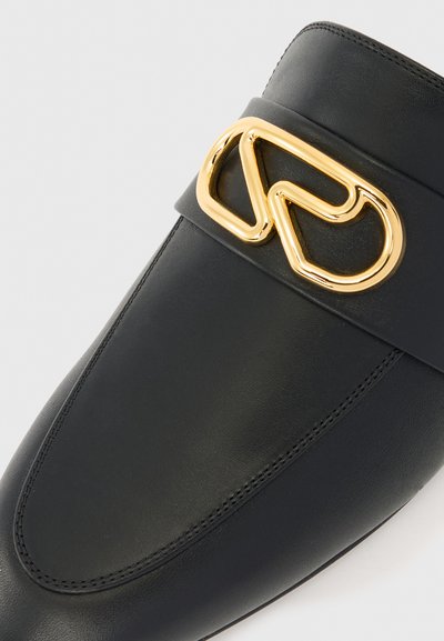 Lofer din piele neagră cu o cataramă din metal, de culoare aurie, cu un design răsucit pe partea superioară, având detalii cusute în zona degetelor.