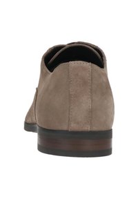 Bruine suède schoenen met een lage hak, strakke lijnen en een gladde textuur; het achteraanzicht benadrukt minimale stiksels en een eenvoudig ontwerp.