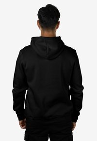 Sudadera con capucha negra de tela suave, con una capucha grande, mangas largas y un dobladillo acanalado. Sin logotipos ni patrones visibles.