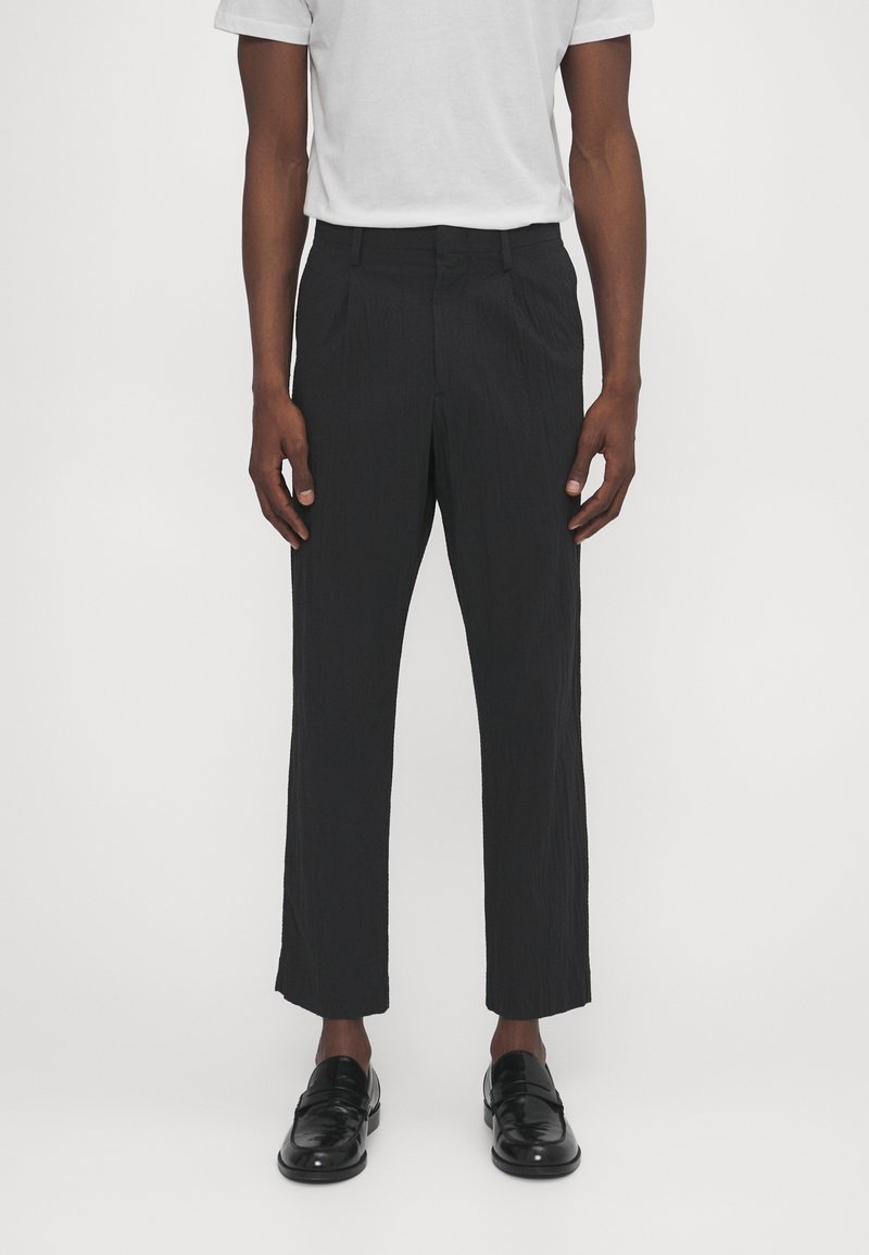 Svarta, texturerade byxor med rak passform, utrustade med en vanlig midja och framfållar, matched med glänsande svarta loafers.