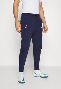 Navy blue Nike joggers with an elastic waistband, drawstring, front pockets, and a Spurs logo embroidered on the left thigh.