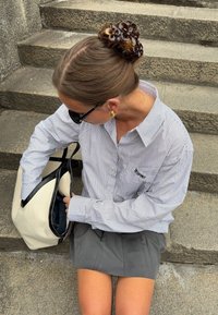 Camisa de botones a rayas, falda gris con pliegues, gafas de sol negras y un bolso crema con detalles en negro. Pelo recogido con un clip floral marrón.