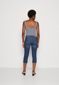 Randig ärmlös bodysuit i kombination med korta mörkblå jeans. Jeansen har bakfickor och medelhög midja. Slät textur.