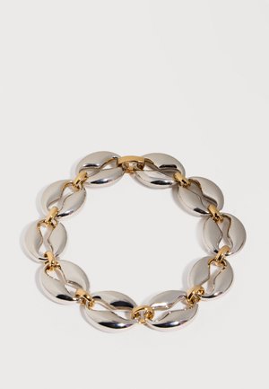 Náramok z kruhovej retiazky spájanej striebrom a zlatom, s hladkými, širokými článkami v tvare disku na jednoduchom bielom pozadí.
