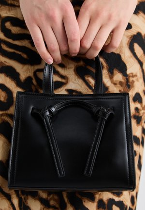 Manos sosteniendo un pequeño bolso de cuero negro sobre un fondo de tela con estampado de leopardo.