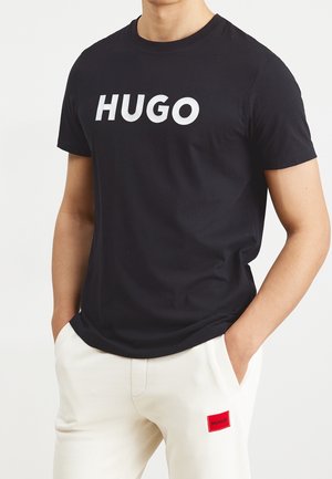 Czarny bawełniany t-shirt z dużym białym logo "HUGO" z przodu. Połączony z białymi spodniami z małą czerwoną metką "HUGO".