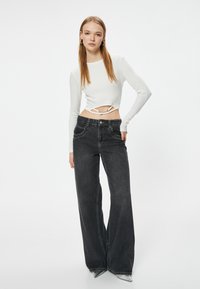 Top corto blanco de manga larga con un corte en la cintura, combinado con jeans de pierna ancha negros de cintura alta que presentan bolsillos delanteros y costuras en contraste.