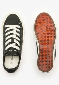 Sneaker nera in tela con lacci bianchi, suola in gomma e accenti beige a contrasto. Motivo del battistrada dettagliato sulla suola. Logo del marchio visibile.