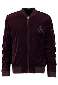 Giacca bomber in velluto bordeaux con zip frontale, polsini e orlo a coste, caratterizzata da una grafica a triangolo e dettagli testuali sulla manica.