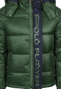Green puffer jacket with navy accent. Features quilted texture, shiny material, front zip, snap buttons, and "POLO PLAYER" logo on the side.
