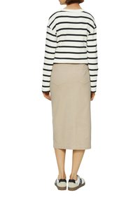 Pull cropped rayé noir et blanc, jupe beige длины колена, et baskets blanches avec des accents noirs et des semelles texturées.