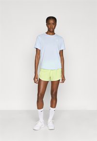 Ανοιχτό μπλε κοντομάνικο μπλουζάκι με μικρό λογότυπο, σετ με αθλητικά σορτς σε νέον πράσινο. Λευκές κάλτσες και παπούτσια ολοκληρώνουν το ντύσιμο.