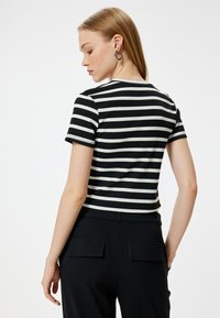 Top de manga corta a rayas blanco y negro con textura acanalada, que presenta un diseño ajustado y un escote redondo. Se lleva con pantalones negros.