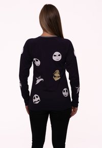 Long-sleeve black shirt with various ghostly faces printed in white and gold. Features a crew neckline and fitted design with ribbed cuffs.