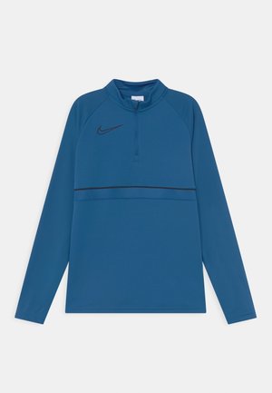 Niebieska długorękawowa koszulka sportowa z pół-zapięciem, lekki materiał, czarne logo Nike powyżej poziomego teksturowanego panelu.