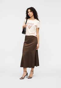 Μπεζ μπλουζάκι με κόκκινο τριγωνικό λογότυπο, σε συνδυασμό με καφέ σατέν μίντι φούστα. Μαύρα ψηλοτάκουνα σανδάλια με λουράκια ολοκληρώνουν την εμφάνιση.