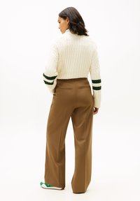Kremowy sweter z grubym splotem warkoczowym, z zielonymi i białymi paskami na rękawach, zestawiony z brązowymi szerokimi spodniami. Gładka tkanina, luźny krój.