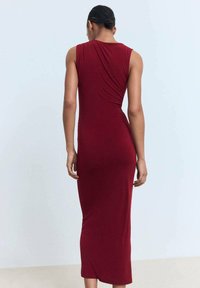 Robe sans manches, longueur genou, en tissu rouge profond, présentant un détail froncé à l'arrière, texture douce et silhouette ajustée.