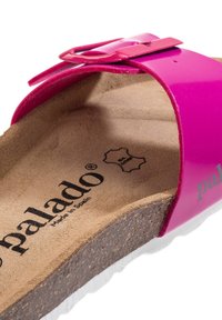 Rosa patentlädersandaler med bred rem, som har en metallspänne och en korkfotbädd. Logotexten säger "palado" med "Tillverkad i Spanien."