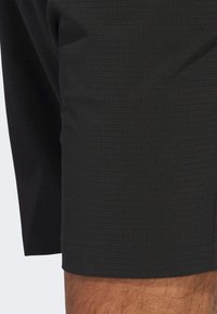 Svarta träningsshorts med ett texturerat rutmönster. Tyget är slätt och sitter tajt runt lårområdet.