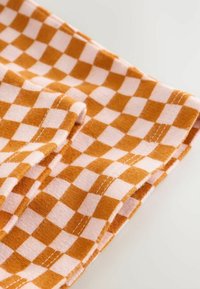 Tkanina w kratkę w kolorze pomarańczowym i różowym, charakteryzująca się miękką fakturą i widocznym przeszyciem. Wzór składa się z naprzemiennych kwadratów.