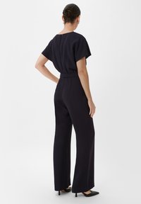 Marineblauer Jumpsuit mit kurzen Ärmeln, elastischem Bund und weitem Bein, ausgestattet mit einem Reißverschluss am Rücken und einer glatten Stofftextur.