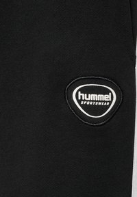 Tissu de sport noir avec un petit patch logo blanc Hummel et une bande blanche verticale le long du bord droit.