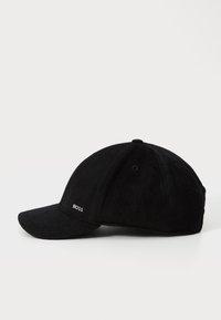Svart ullcaps med buet skygge, seks paneler, og brodert logo på venstre side. Myk tekstur og strukturert design.
