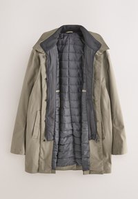 Long manteau beige à devant ouvert révélant une doublure intérieure matelassée gris foncé et un col, étalé à plat sur un fond clair.