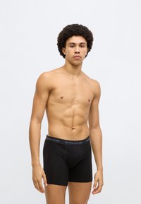 Sort boxershorts lavet af blødt stof med en bred linning med "TOMMY HILFIGER" branding i hvidt og rødt, tætsiddende pasform, glat tekstur.