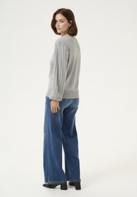 Light gray knitted sweater with ribbed puff sleeves, worn with high-waisted blue wide-leg jeans and black block-heeled shoes.