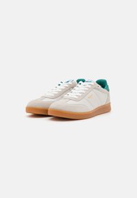 Zapatillas de ante blancas con acentos verdes y suelas de goma. Presentan cierre con cordones y un forro de tejido texturizado para mayor comodidad.