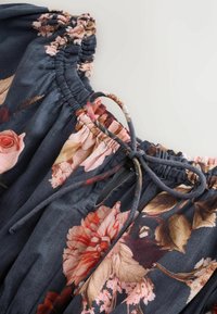 Stofă cu model floral în nuanța albastru marine, având un guler plisat și detalii cu panglică. Textură moale, cu flori vibrante în nuanțe de roz, roșu și crem.